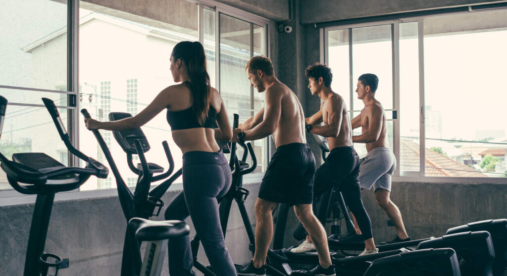 Group of people doing exercises on elliptical machine at gym